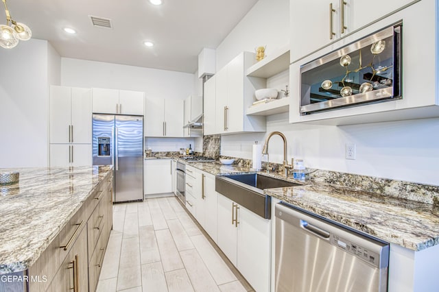 kitchen with sink, white cabinetry, stainless steel appliances, light stone countertops, and decorative backsplash