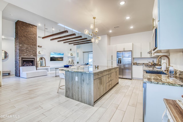 kitchen featuring decorative light fixtures, stainless steel fridge with ice dispenser, a kitchen island, light stone countertops, and white cabinets