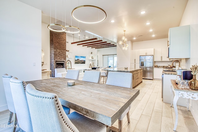 dining room featuring sink, an inviting chandelier, a fireplace, and a towering ceiling