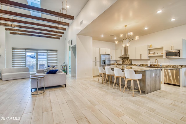 kitchen with appliances with stainless steel finishes, decorative light fixtures, white cabinetry, a center island, and wall chimney range hood