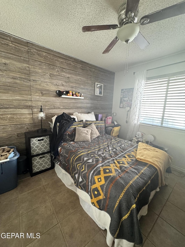 tiled bedroom featuring ceiling fan, a textured ceiling, and wooden walls