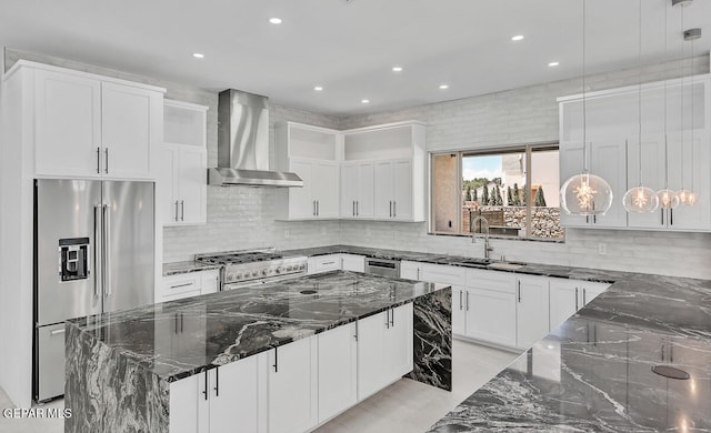 kitchen with wall chimney exhaust hood, high quality appliances, hanging light fixtures, and dark stone countertops