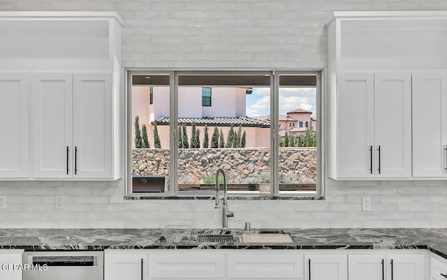 kitchen with tasteful backsplash, white cabinets, dark stone counters, and dishwasher