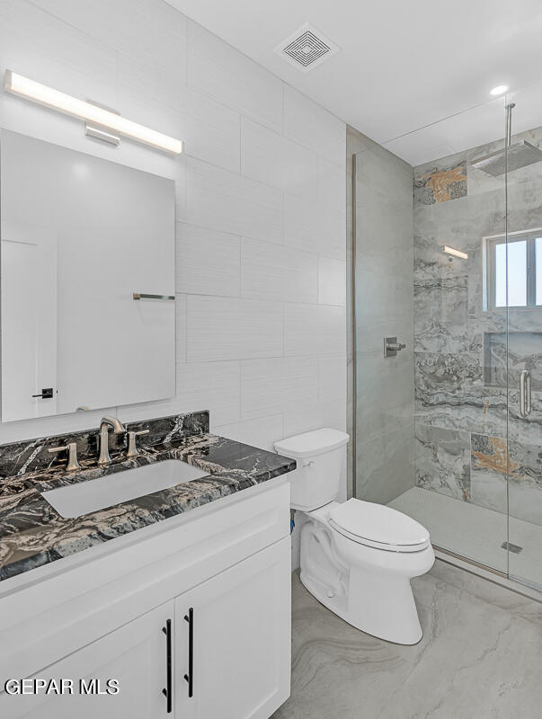 bathroom with vanity, toilet, a shower with shower door, and tile walls