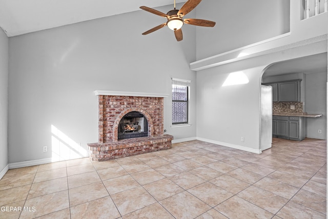 unfurnished living room featuring light tile patterned flooring, ceiling fan, a fireplace, and a high ceiling