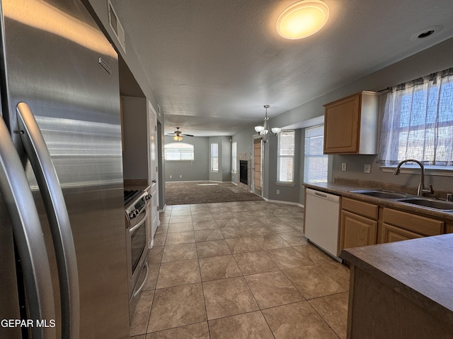 kitchen with light brown cabinetry, a fireplace, sink, light tile patterned floors, and stainless steel appliances