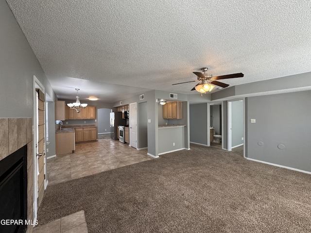 unfurnished living room with sink, a textured ceiling, a tiled fireplace, ceiling fan with notable chandelier, and light colored carpet