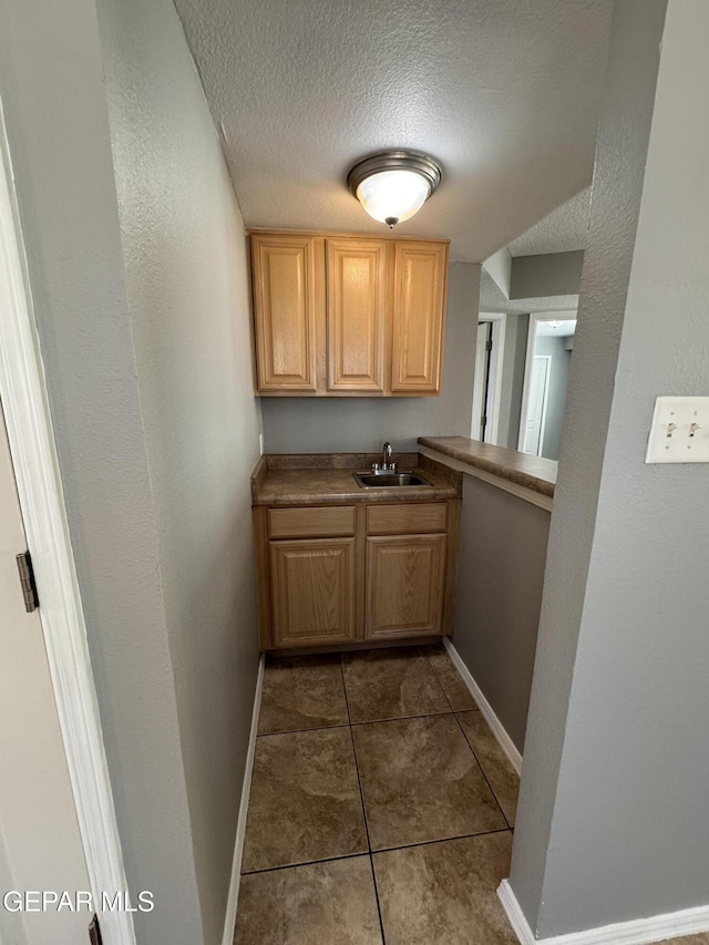 kitchen with sink, dark tile patterned floors, a textured ceiling, and light brown cabinets