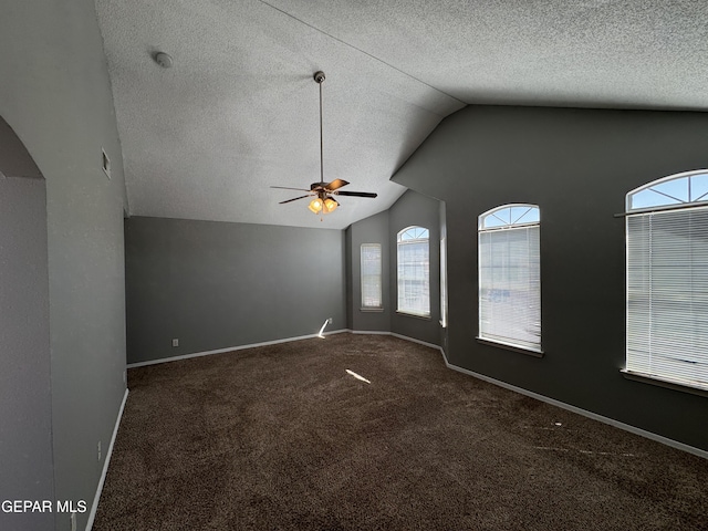 empty room featuring dark carpet, vaulted ceiling, a textured ceiling, and ceiling fan