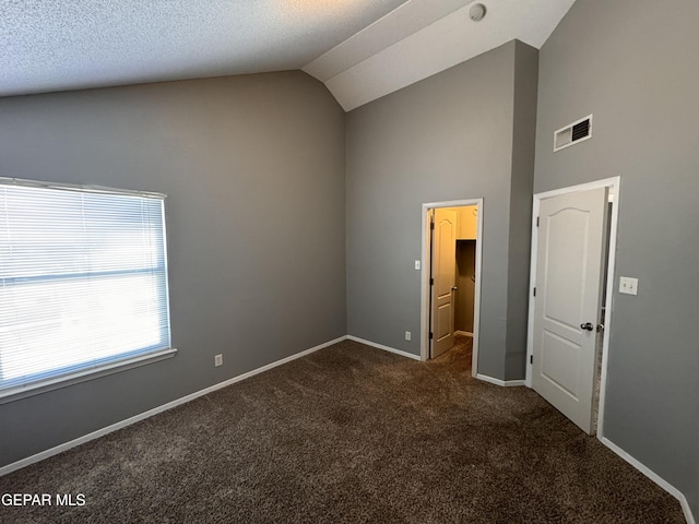 unfurnished bedroom featuring lofted ceiling, a spacious closet, dark carpet, and a textured ceiling