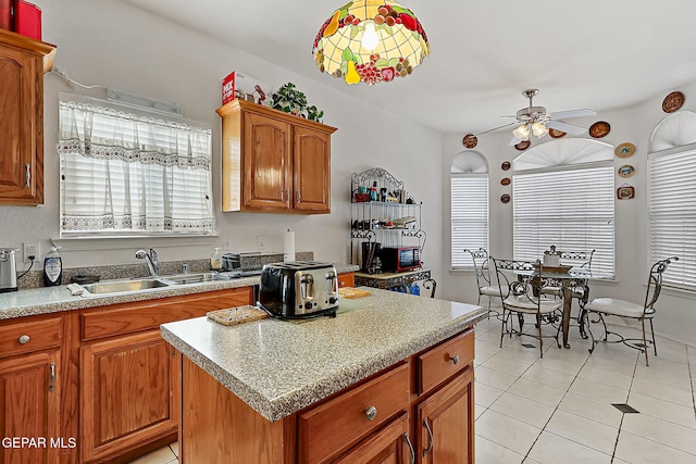 kitchen featuring sink, light tile patterned floors, ceiling fan, a center island, and decorative light fixtures