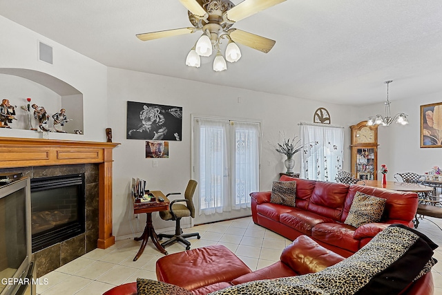 living room with a tiled fireplace, light tile patterned floors, and ceiling fan with notable chandelier