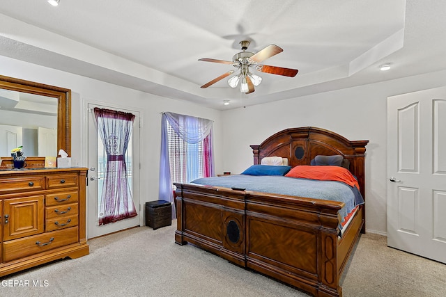 carpeted bedroom with a tray ceiling, access to outside, and ceiling fan