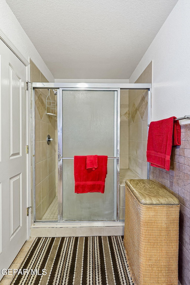 bathroom featuring a shower with shower door, tile patterned flooring, and a textured ceiling