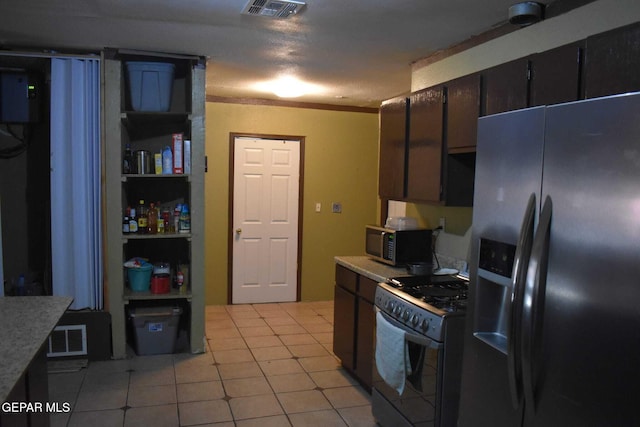 kitchen with light tile patterned flooring, dark brown cabinetry, ornamental molding, stainless steel fridge, and range with gas stovetop