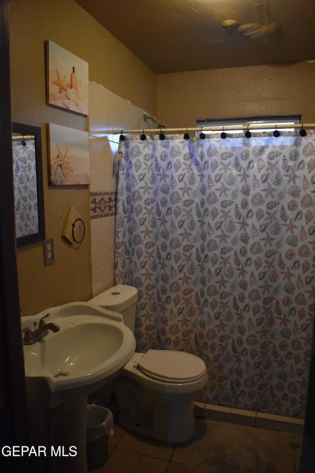 bathroom featuring toilet, walk in shower, sink, and tile patterned flooring