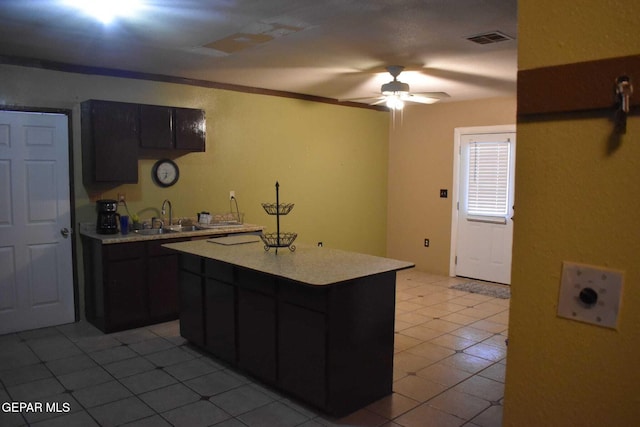 kitchen with sink, light tile patterned floors, ceiling fan, ornamental molding, and a kitchen island