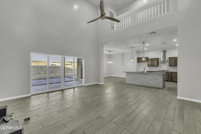 unfurnished living room featuring ceiling fan, wood-type flooring, sink, and a high ceiling