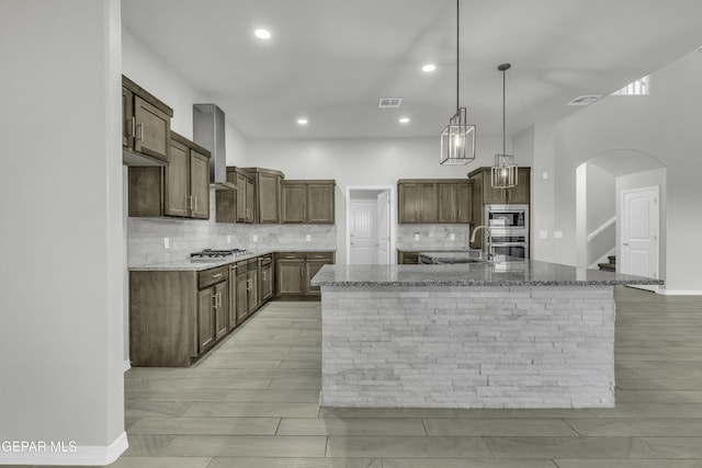 kitchen featuring tasteful backsplash, stainless steel appliances, light stone countertops, and an island with sink