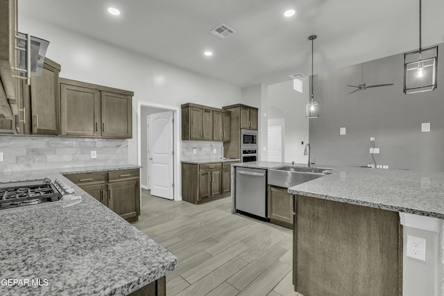 kitchen with light stone counters, decorative light fixtures, an island with sink, and appliances with stainless steel finishes