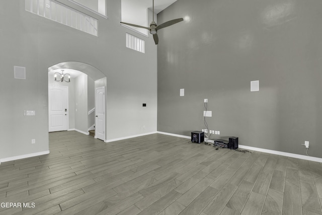 unfurnished living room with wood-type flooring, ceiling fan, and a high ceiling