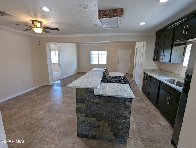 kitchen with a kitchen island, sink, ornamental molding, ceiling fan, and light stone counters