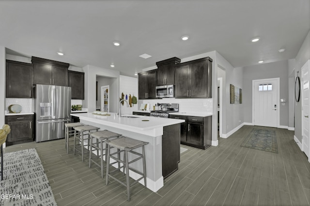 kitchen with sink, a breakfast bar, appliances with stainless steel finishes, a center island with sink, and decorative backsplash