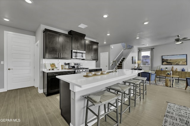 kitchen featuring tasteful backsplash, appliances with stainless steel finishes, a kitchen breakfast bar, and a center island with sink