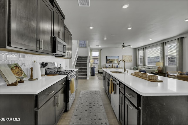 kitchen with sink, tasteful backsplash, a center island with sink, appliances with stainless steel finishes, and ceiling fan