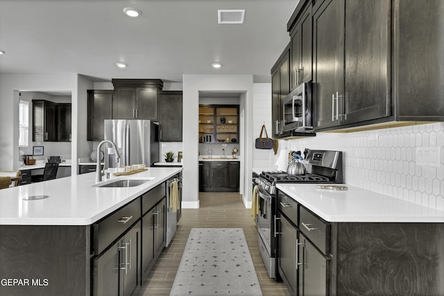 kitchen featuring stainless steel appliances, a kitchen island with sink, sink, and decorative backsplash