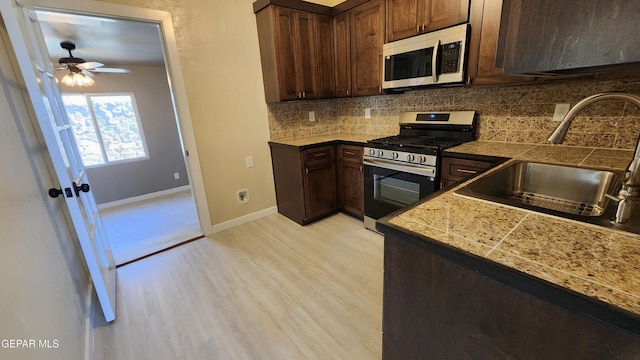 kitchen with dark brown cabinetry, sink, tasteful backsplash, light wood-type flooring, and appliances with stainless steel finishes