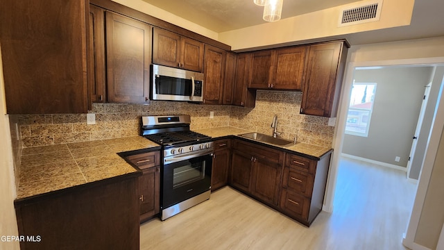 kitchen featuring sink, appliances with stainless steel finishes, dark brown cabinetry, decorative backsplash, and light wood-type flooring