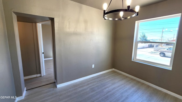 empty room with wood-type flooring and a notable chandelier