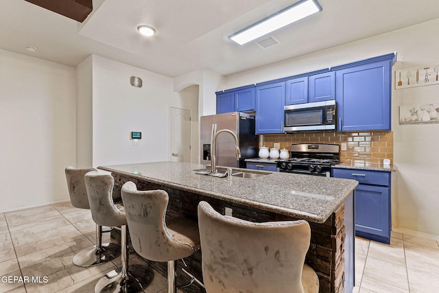 kitchen featuring blue cabinets, a breakfast bar, tasteful backsplash, appliances with stainless steel finishes, and an island with sink