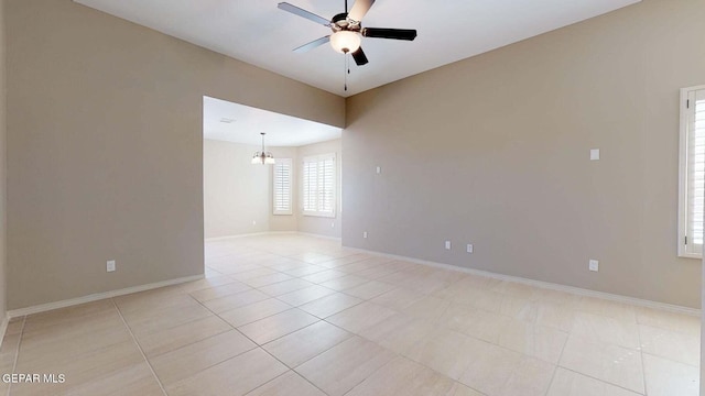 empty room with ceiling fan with notable chandelier and light tile patterned floors