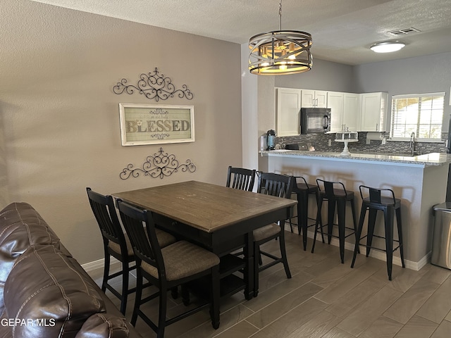 dining area featuring wood-type flooring, a chandelier, sink, and a textured ceiling