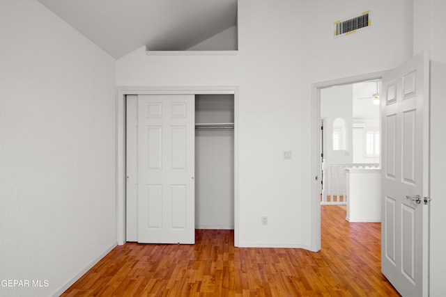 unfurnished bedroom with a closet, high vaulted ceiling, and light hardwood / wood-style flooring