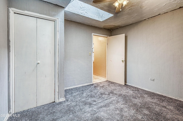 unfurnished bedroom featuring a closet, carpet floors, ceiling fan, and a skylight