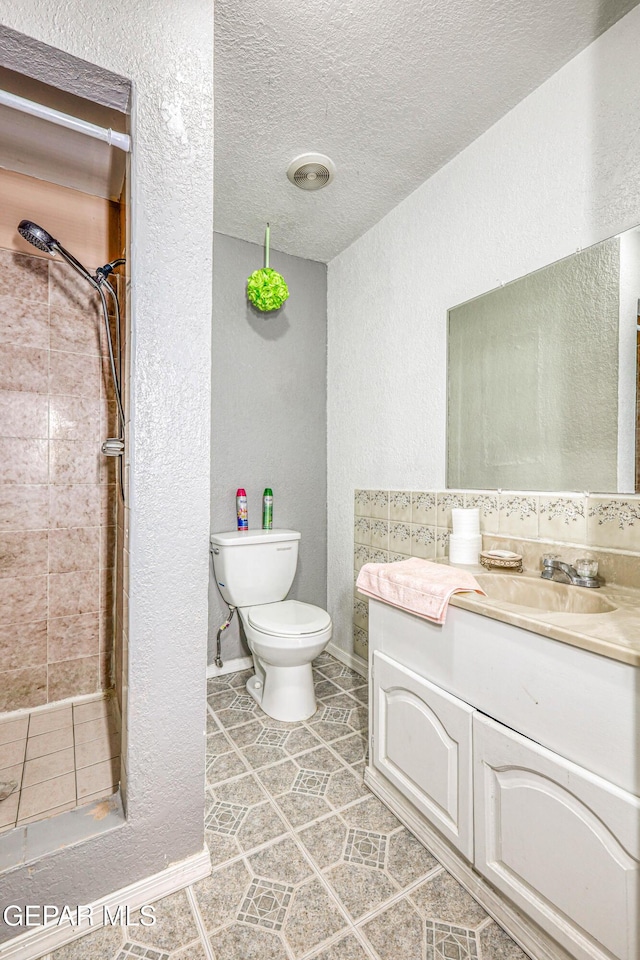 bathroom featuring vanity, toilet, a textured ceiling, and tiled shower