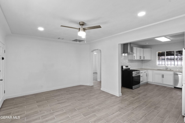 kitchen with wall chimney exhaust hood, white cabinetry, appliances with stainless steel finishes, ceiling fan, and backsplash