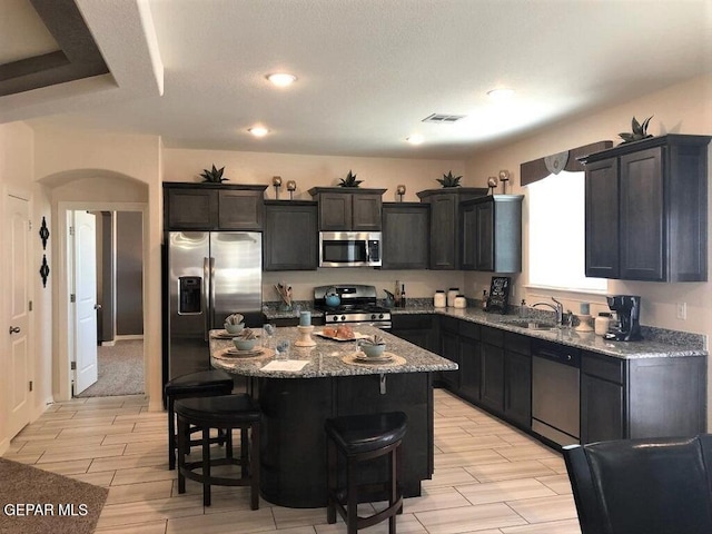 kitchen featuring a center island, arched walkways, a breakfast bar, stainless steel appliances, and visible vents