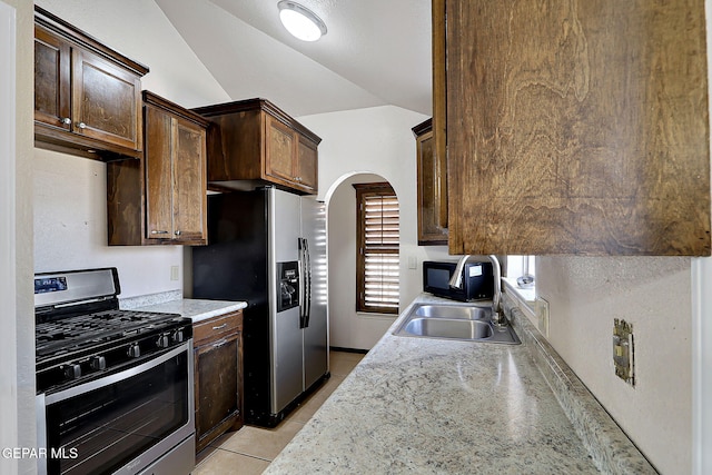 kitchen with light tile patterned flooring, vaulted ceiling, sink, dark brown cabinetry, and stainless steel appliances