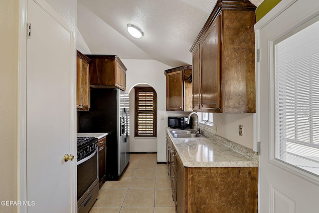 kitchen with lofted ceiling, sink, stainless steel range with gas stovetop, a textured ceiling, and light tile patterned flooring