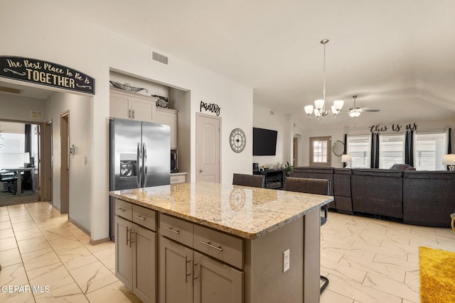 kitchen with a kitchen island, pendant lighting, ceiling fan with notable chandelier, light stone counters, and stainless steel refrigerator with ice dispenser