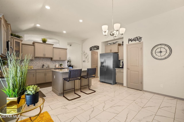 kitchen featuring a kitchen island, lofted ceiling, stainless steel fridge, backsplash, and a notable chandelier