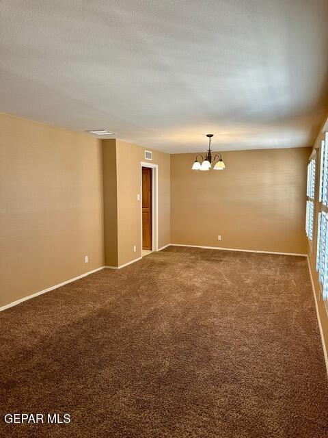 spare room with an inviting chandelier, carpet flooring, and a textured ceiling