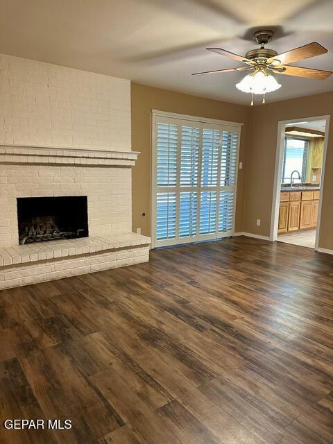 unfurnished living room featuring dark wood-type flooring, ceiling fan, sink, and a brick fireplace