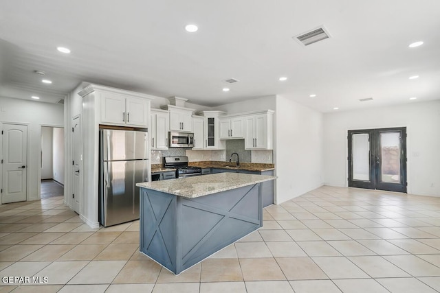 kitchen featuring white cabinets, backsplash, light tile patterned floors, stainless steel appliances, and light stone countertops