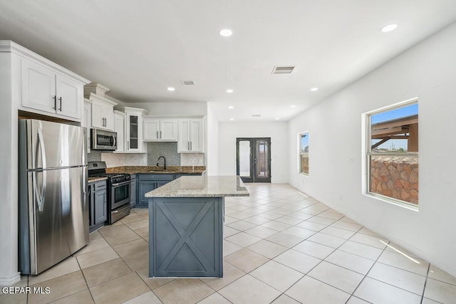 kitchen with sink, appliances with stainless steel finishes, white cabinetry, a center island, and light stone countertops