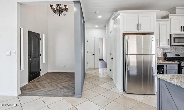 kitchen with white cabinetry, stainless steel appliances, light stone countertops, light parquet floors, and backsplash